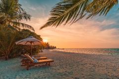Sun setting over a beach with lounge chairs and beach umbrella